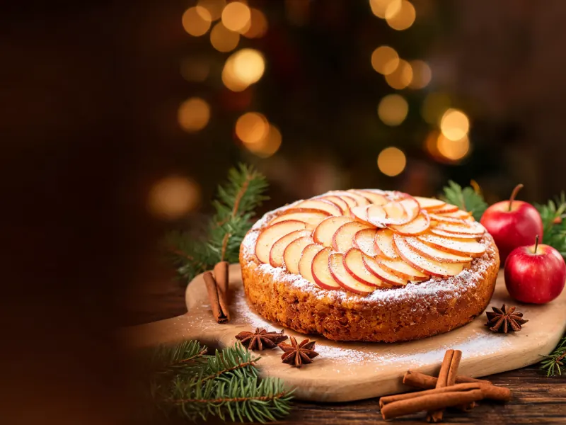 Apfel-Zimt-Kuchen mit Apfelspalten und Puderzucker, daneben Zimtstangen und Tannenzweige (KI-generiertes Bild)