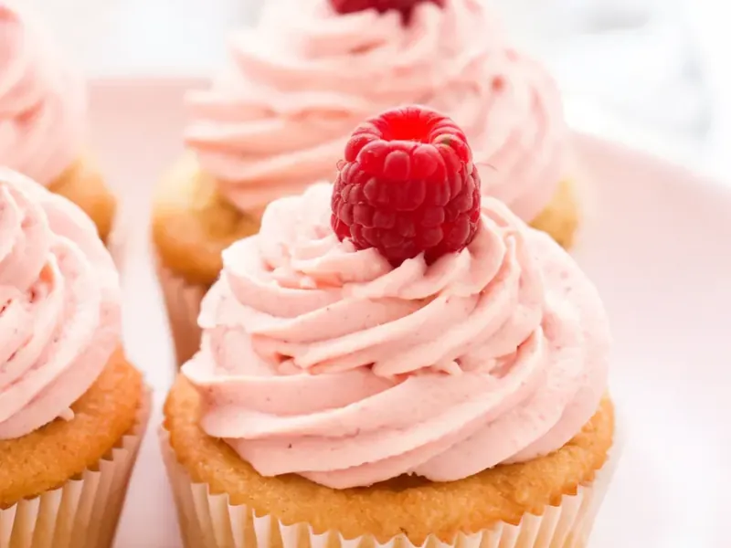 Vanille-Cupcakes mit rosa Himbeer-Frosting und Himbeeren (KI-generiertes Bild)