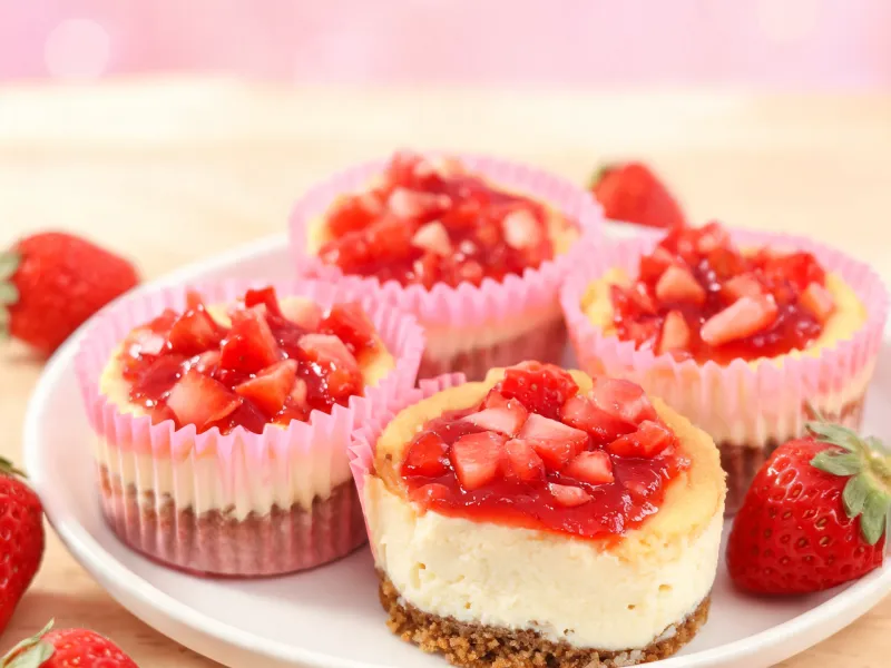 Käsekuchen-Muffins mit Keksboden und Erdbeer-Topping in rosa Papierförmchen (KI-generiertes Bild)