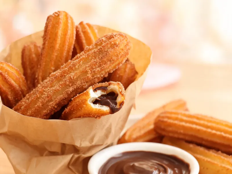 Goldene Churros in Zimtzucker, einer aufgebrochen mit Schokoladenfüllung (KI-generiertes Bild)