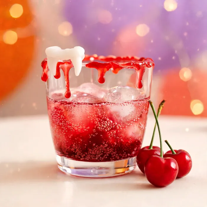 Roter Kirsch-Sprudel mit tropfendem rotem Zuckerrand und Gummi-Vampirzähnen (KI-generiertes Bild)