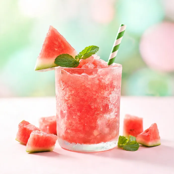 Eisiger pinker Wassermelonen-Slush mit Melonenstück am Glasrand (KI-generiertes Bild)