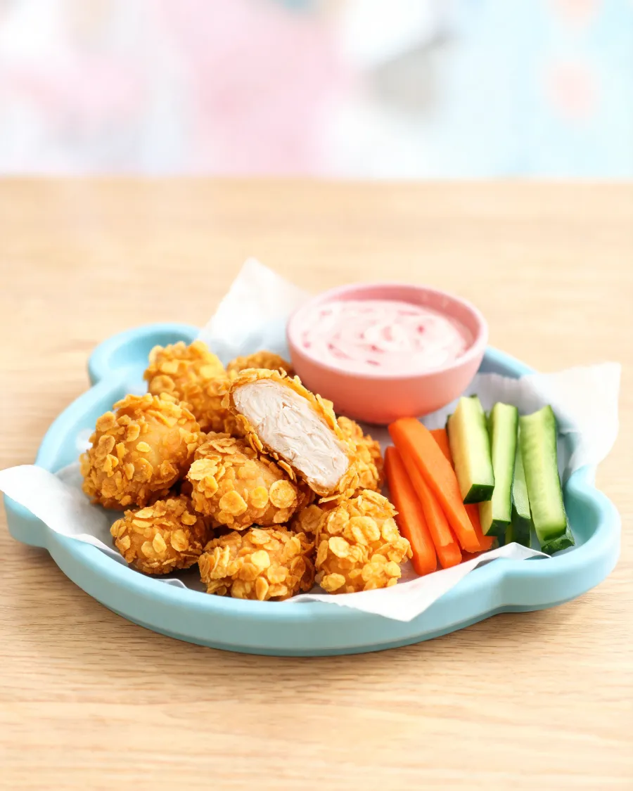 Chicken-Nuggets mit Cornflakes-Panade, einer aufgeschnitten, mit rosa Dip und Gemüsesticks (KI-generiertes Bild)