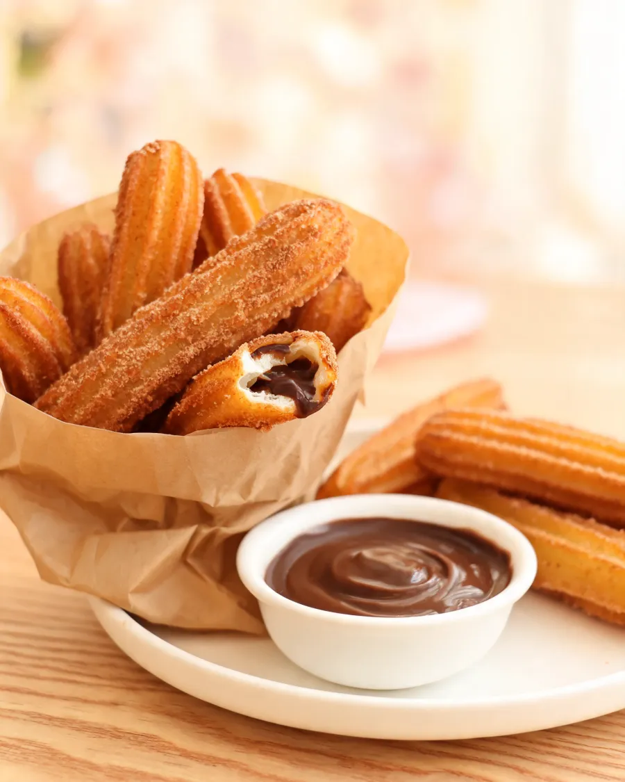 Goldene Churros in Zimtzucker, einer aufgebrochen mit Schokoladenfüllung (KI-generiertes Bild)